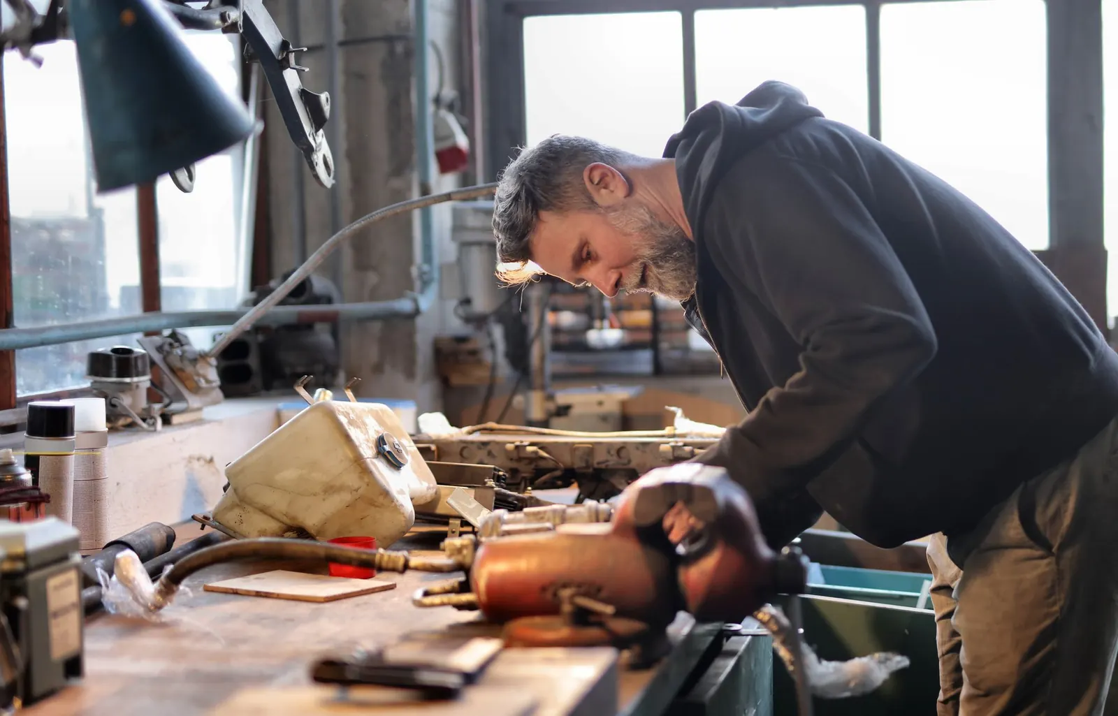 A workshop owner at his bench fixing metal parts with hand tools